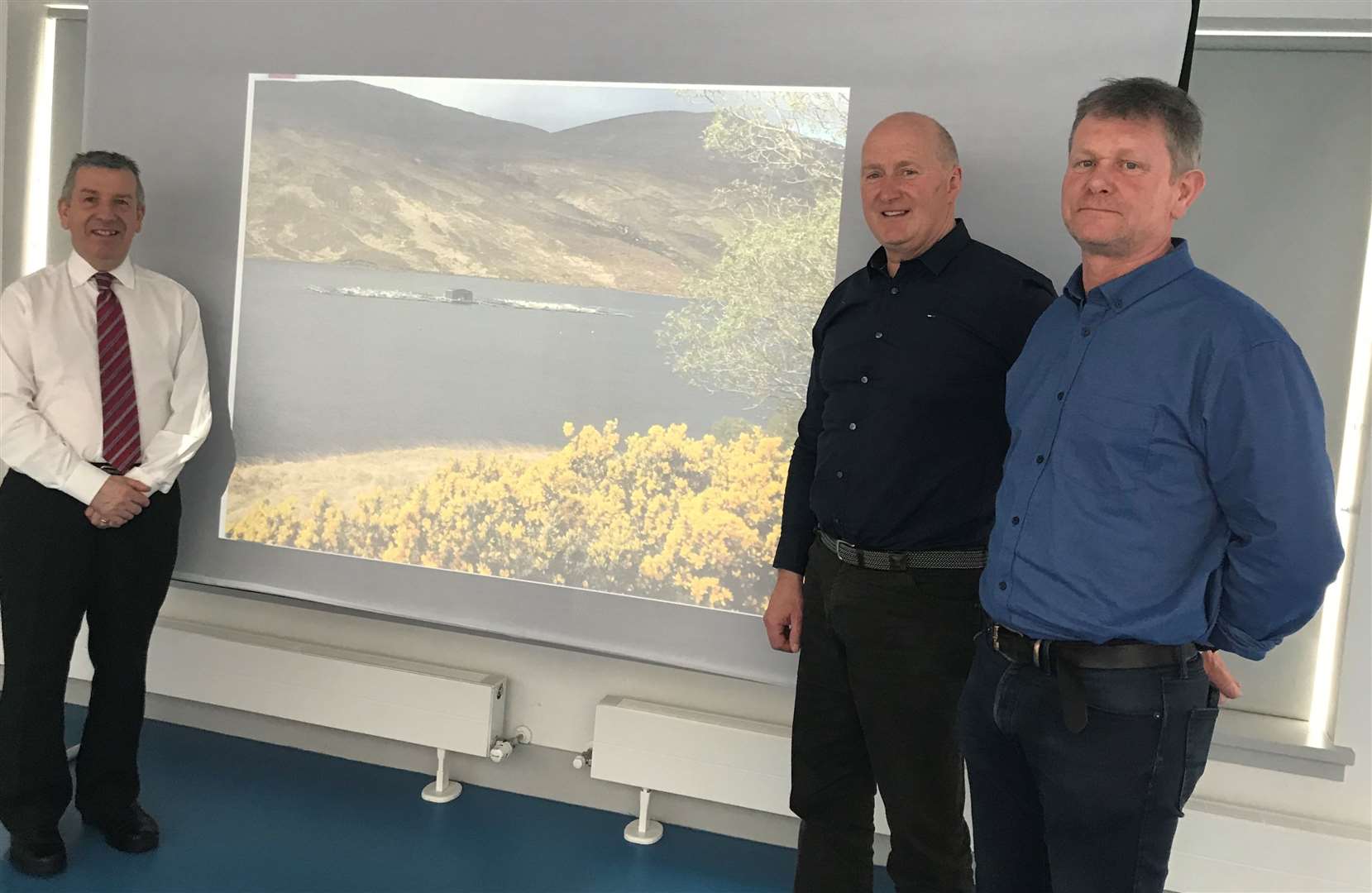 David Stewart (left) with Hugh Murray and David Catto (right) and, in the background, a photo of one of the company’s sites on Loch Merkland.