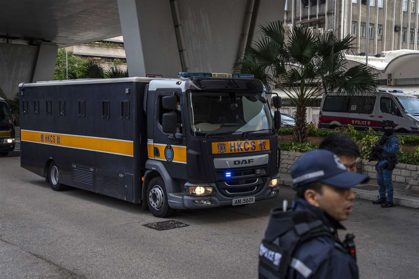 Police stand guard as a vehicle believed to be carrying activist publisher Jimmy Lai arrives at West Kowloon Magistrates’ Courts (Vernon Yuen/AP)