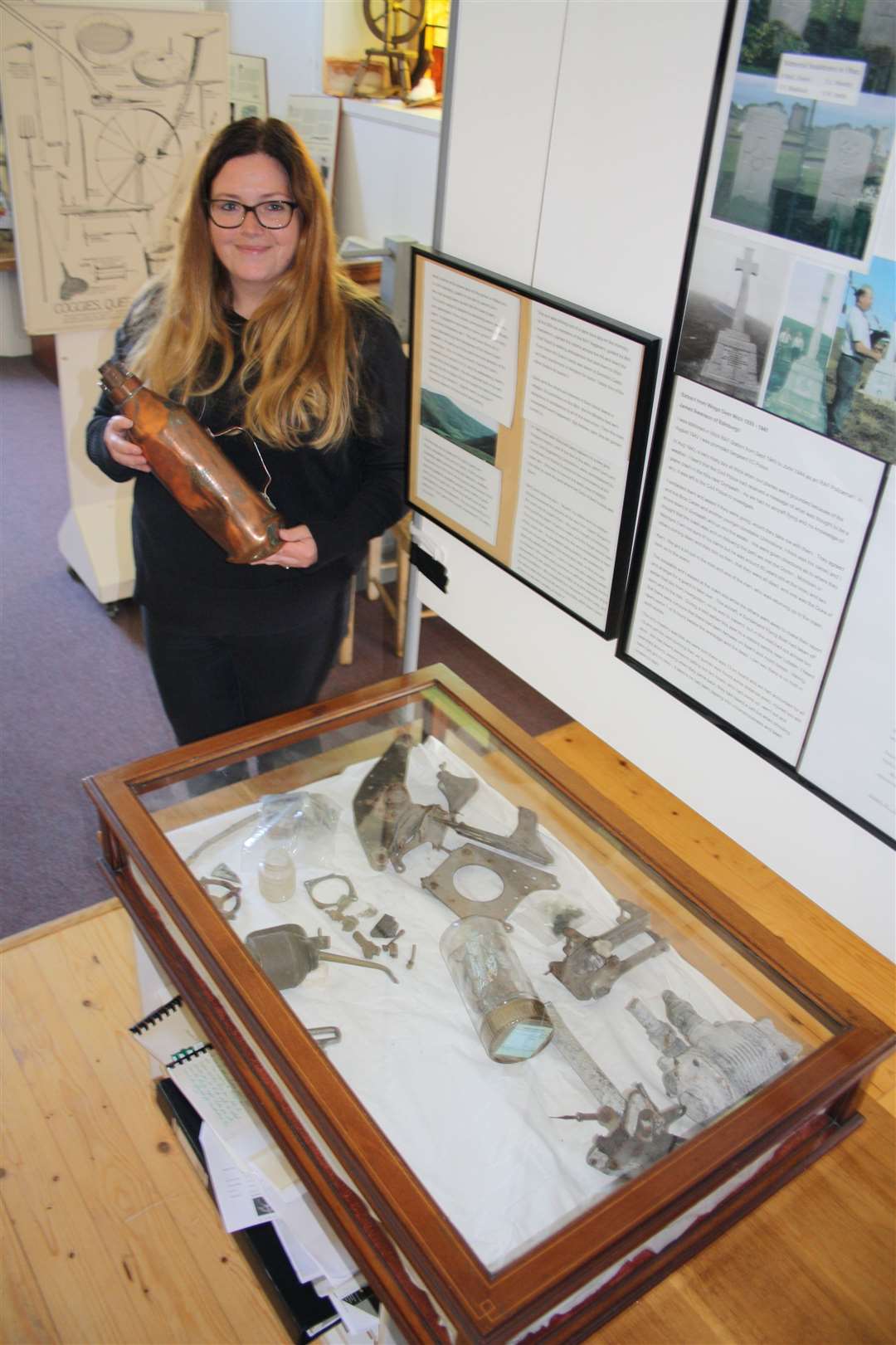 Liza Gordon, development officer, Dunbeath Heritage Centre, holds fire extinguisher from crash site as she stands by cabinet of other artefacts.