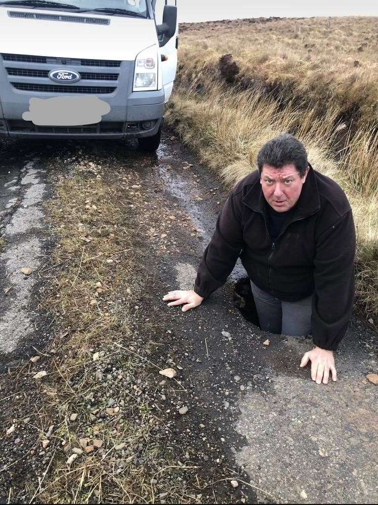 Cape Wrath mini-bus operator Stuart Ross climbs into the pothole to show how deep it is.