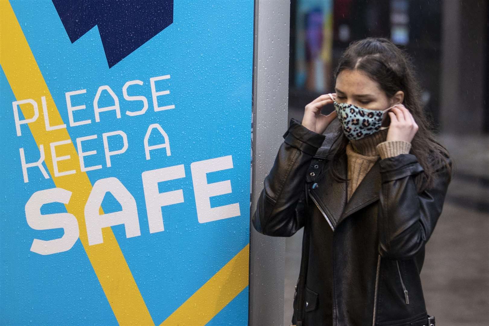 A young woman puts on her face covering as she walks past a Covid-19 safety message from Belfast City Council (Liam McBurney/PA)