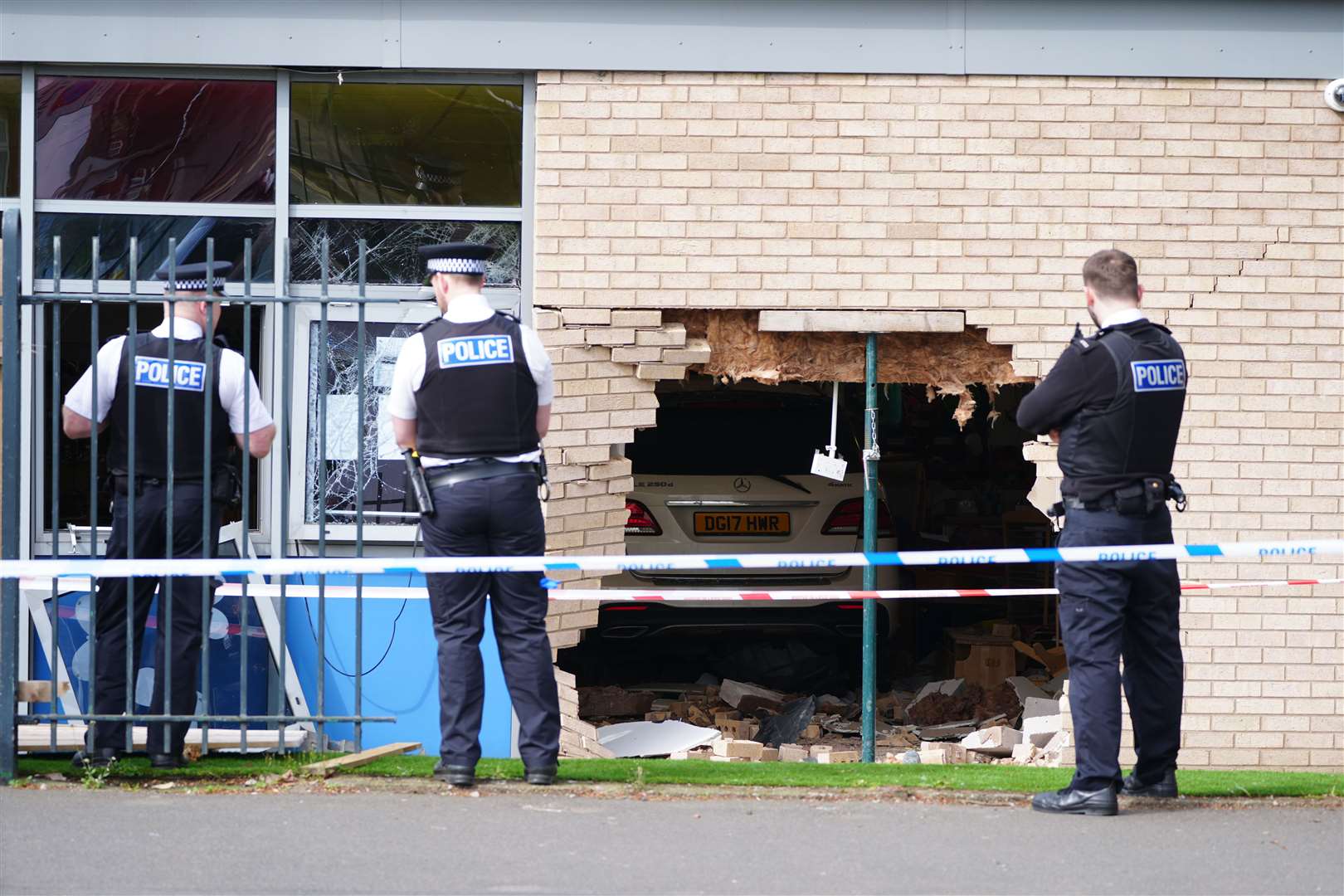 Police officers stand beside the debris and damage after a car crashed through a wall at Beacon Church of England Primary School (Peter Byrne/PA)