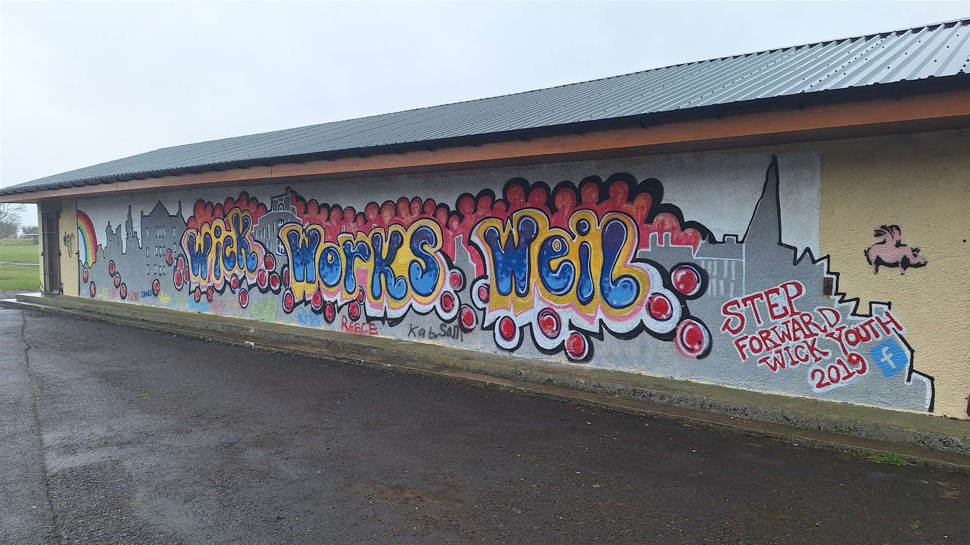 Wick Works Weil graffiti on building in riverside car park.