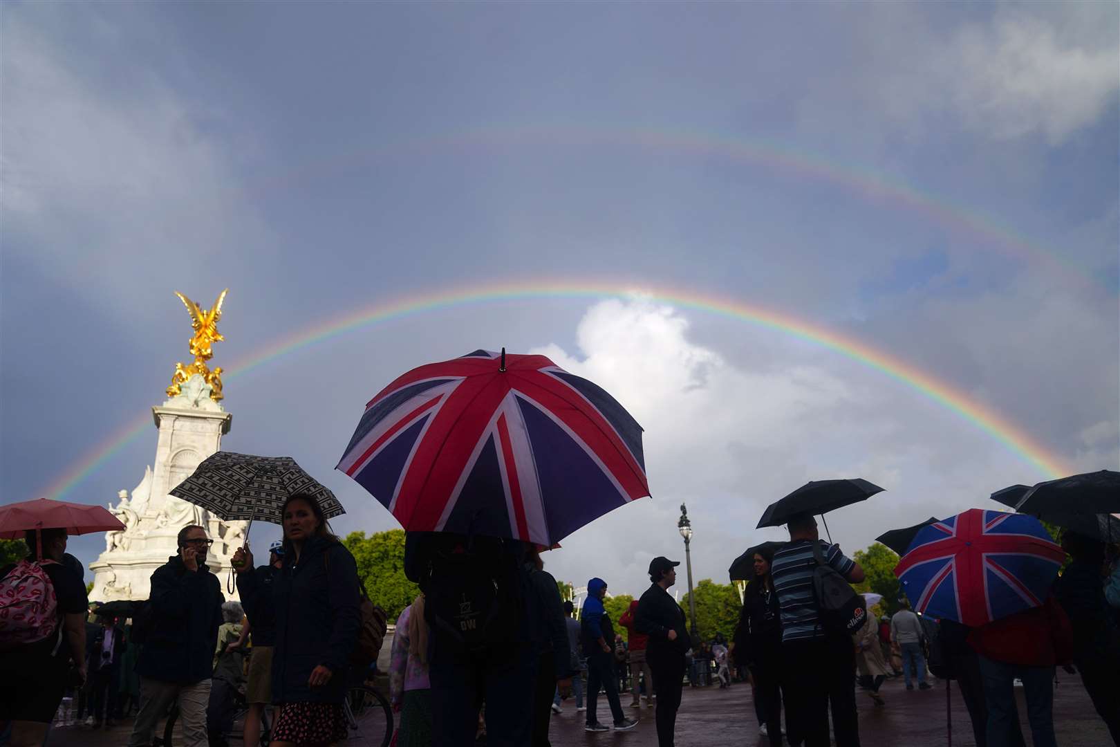 A rainbow is seen, as members of the public gather outside Buckingham Palace (Victoria Jones/PA)