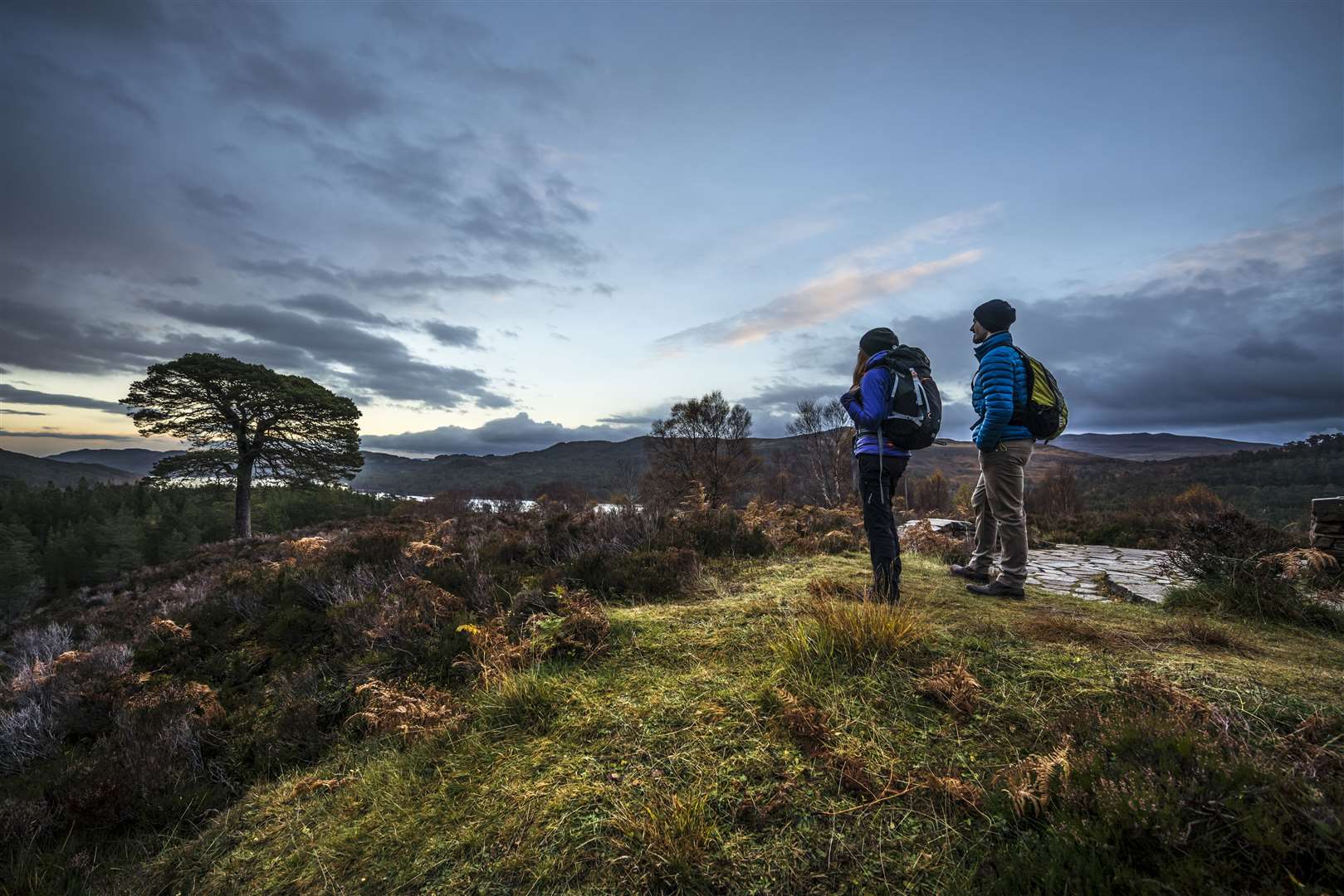 A couple of walkers standing looking over the landscape of the national nature reserve, river and moorland in the Glen Affric area.