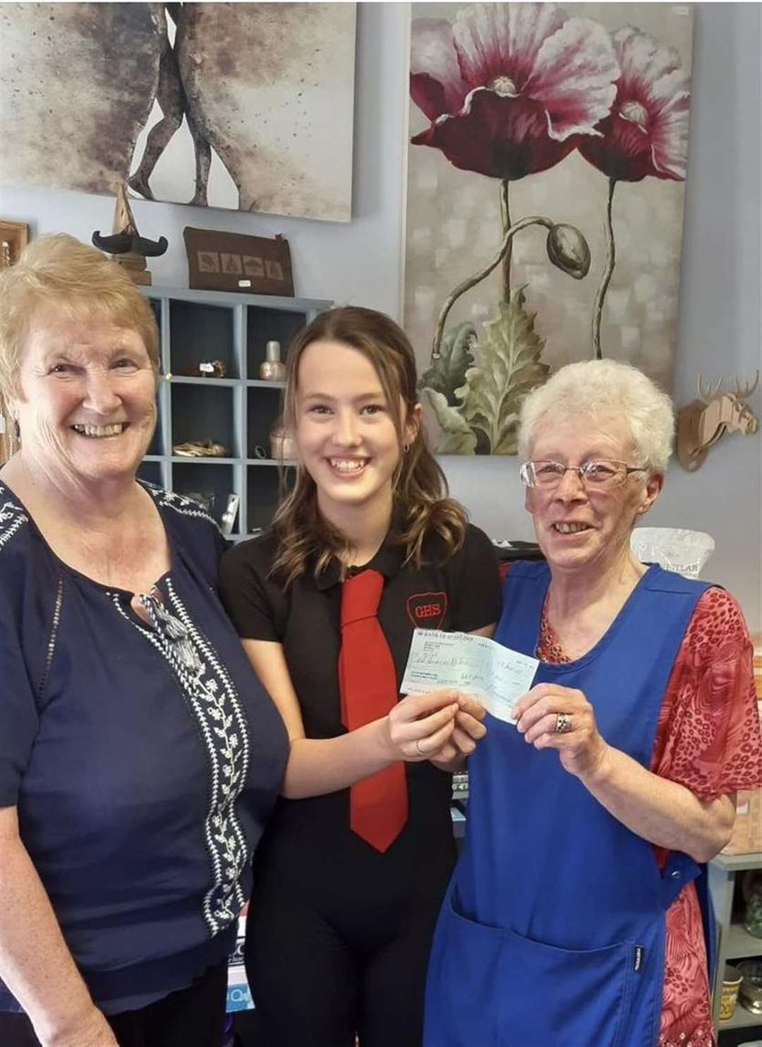 Poppy Mackay presents the £150 cheque she received for her nominated charity as part of her award to TYKES shop volunteers Moura Campbell and Marie Macleod.