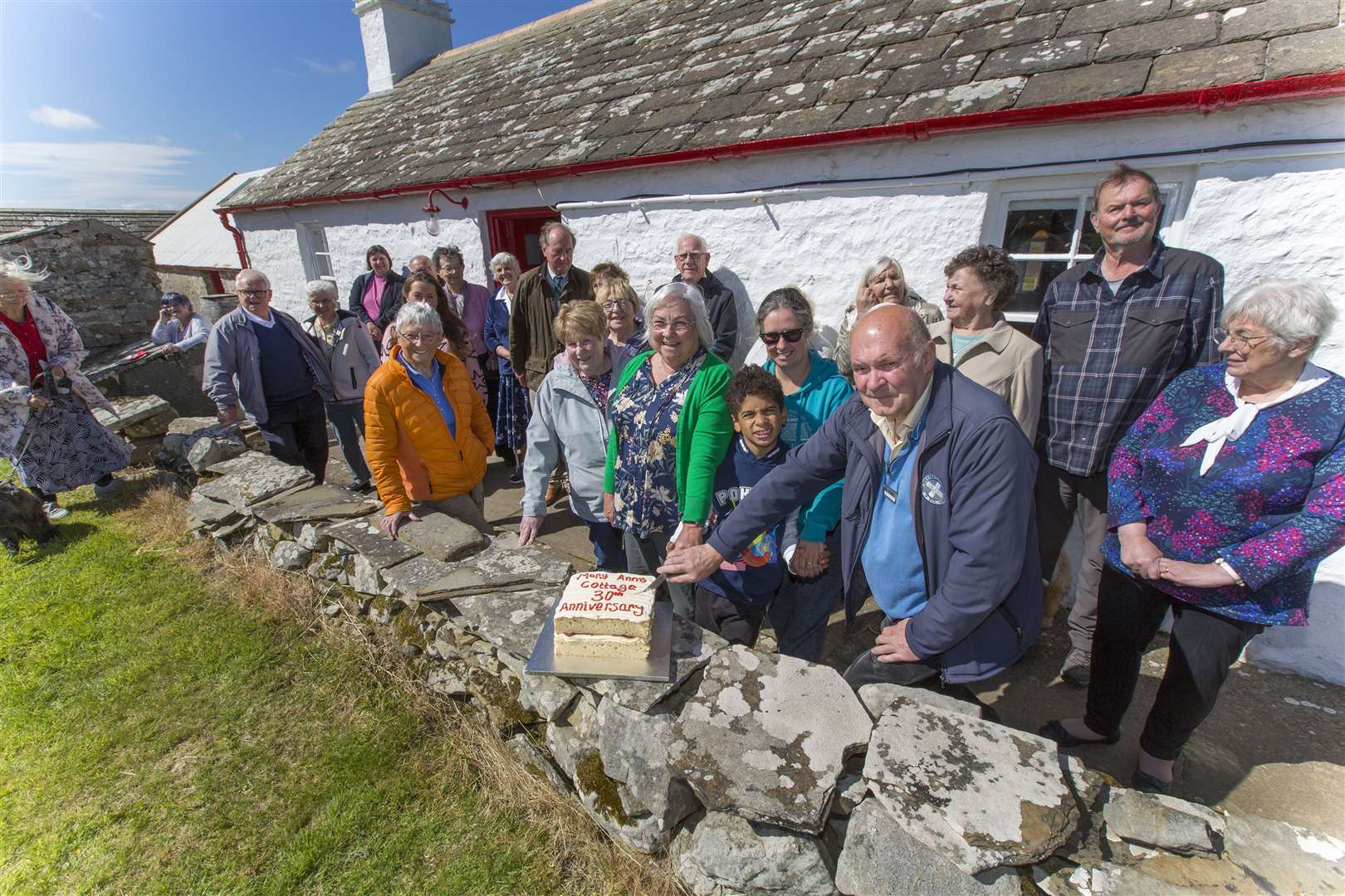 Mary-Ann's granddaughter Anne Fitzsimmons, great-granddaughter Claire Fitzsimmons and great-great-grandson Charlie Fitzsimmons, along with Bob Bell, interim chairman of the trust that looks after the cottage, cut the 30th anniversary cake. Looking on are Annette Sinclair (front, fifth from right) and some of the other trustees and volunteers. Picture: Robert MacDonald / Northern Studios