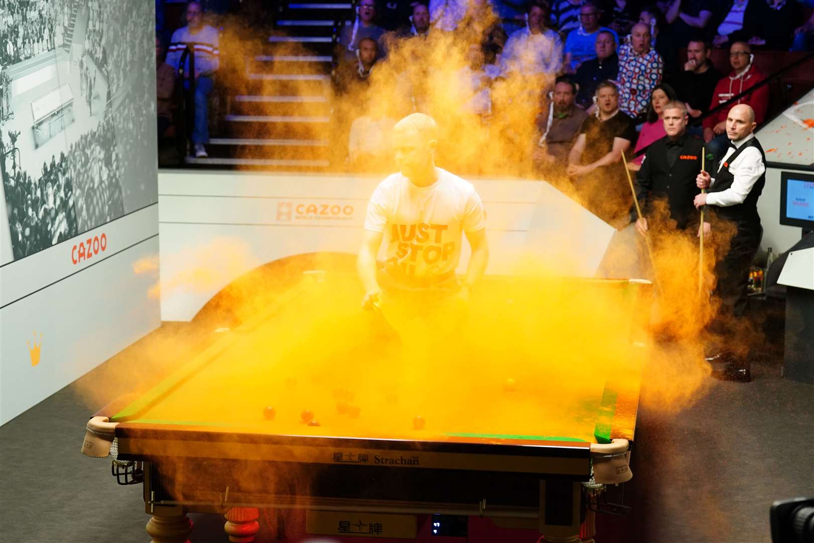 A Just Stop Oil protester jumps on the table and throws orange powder during the match between Robert Milkins against Joe Perry during day three of the Cazoo World Snooker Championship at the Crucible Theatre, Sheffield (Mike Egerton/PA)
