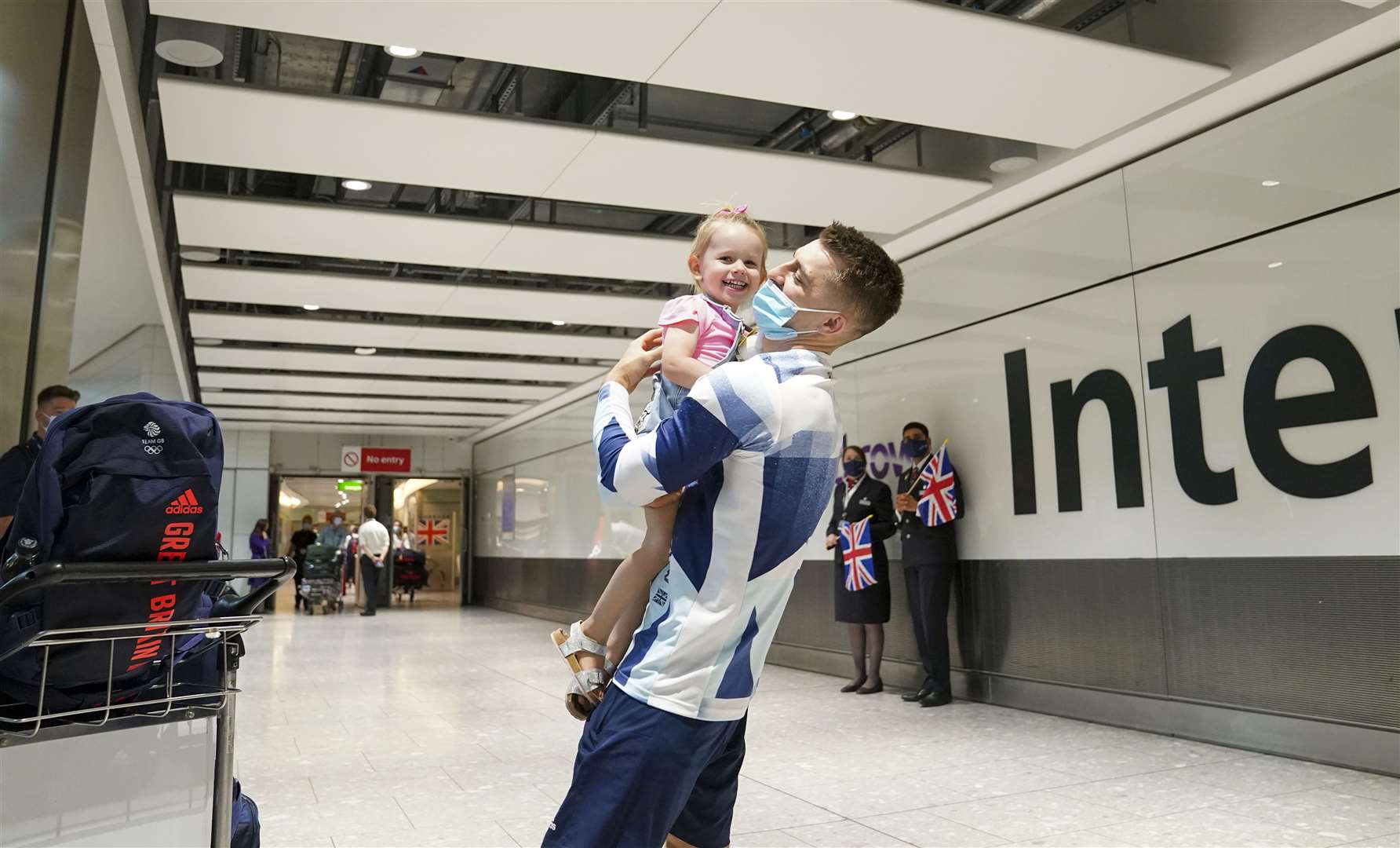 Olympic gymnast Max Whitlock hugs his daughter Willow as he arrives back at London Heathrow Airport (Steve Parsons/PA)