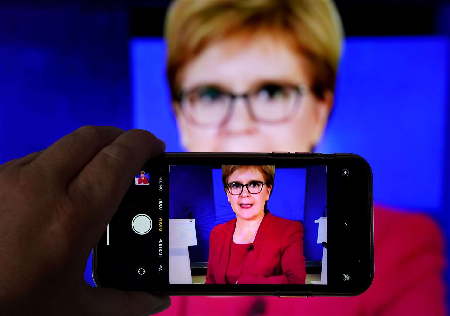 A person uses their phone to film a televised broadcast of First Minister Nicola Sturgeon speaking to MSPs during a virtual sitting of the Scottish Parliament (Andrew Milligan/PA)