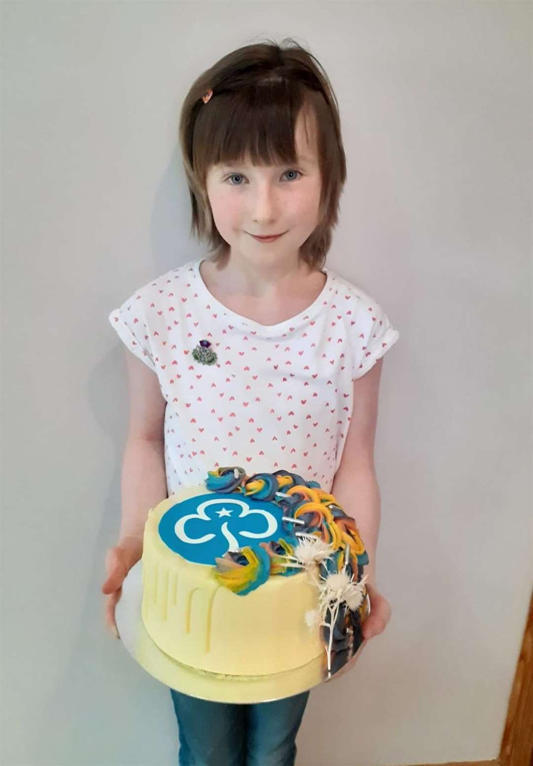 Imogen Gunn, wearing her award, holding a cake she received from Girlguiding Caithness to help her and her family celebrate.