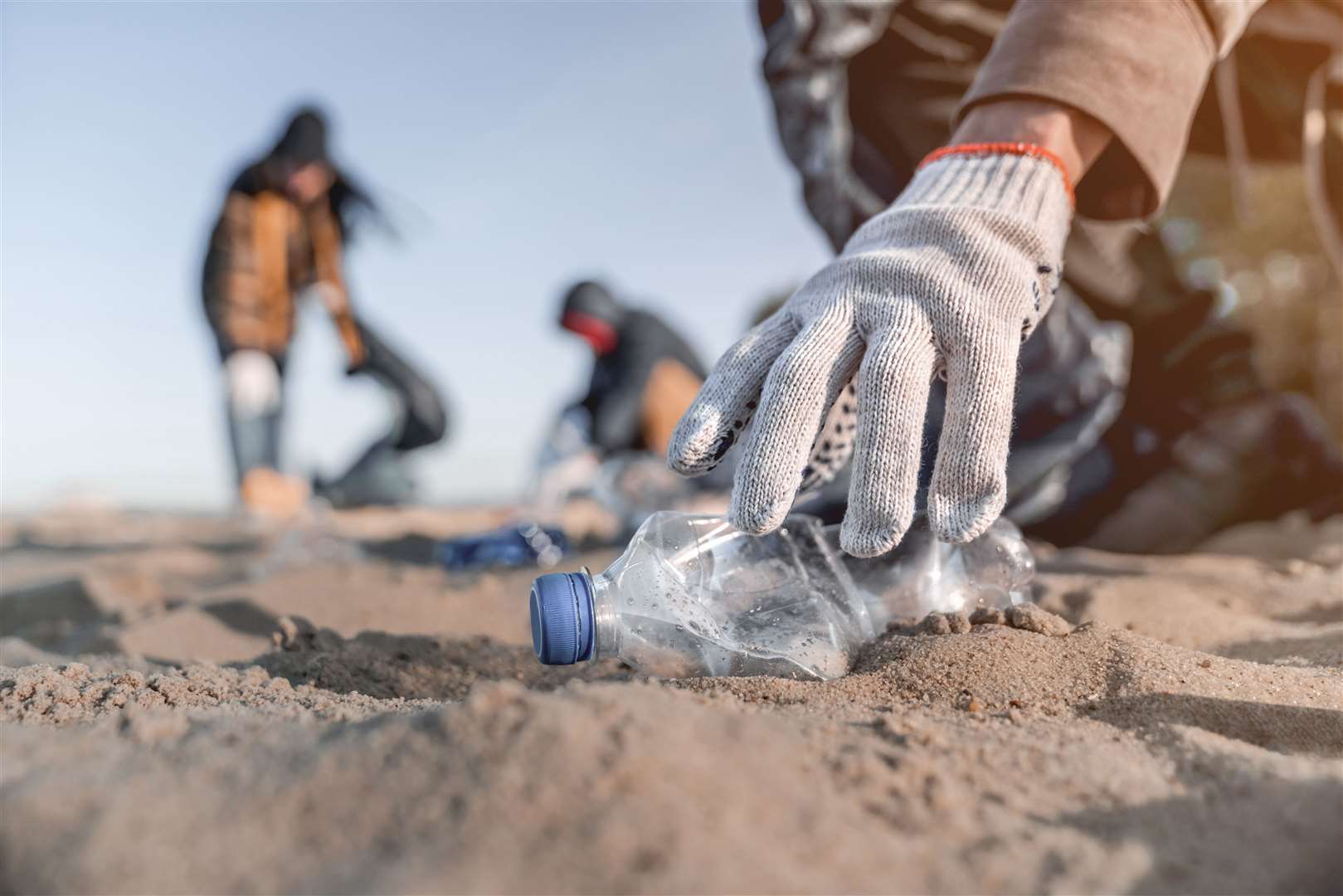 A volunteer beach cleaner picks up a plastic bottle. Picture: Adobe Stock Images